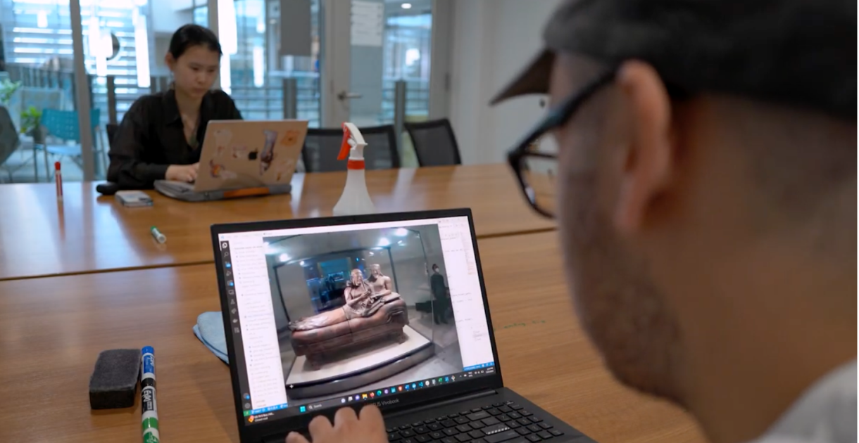 laptop screen image of an art piece viewed over the shoulder of student wearing glasses and hat